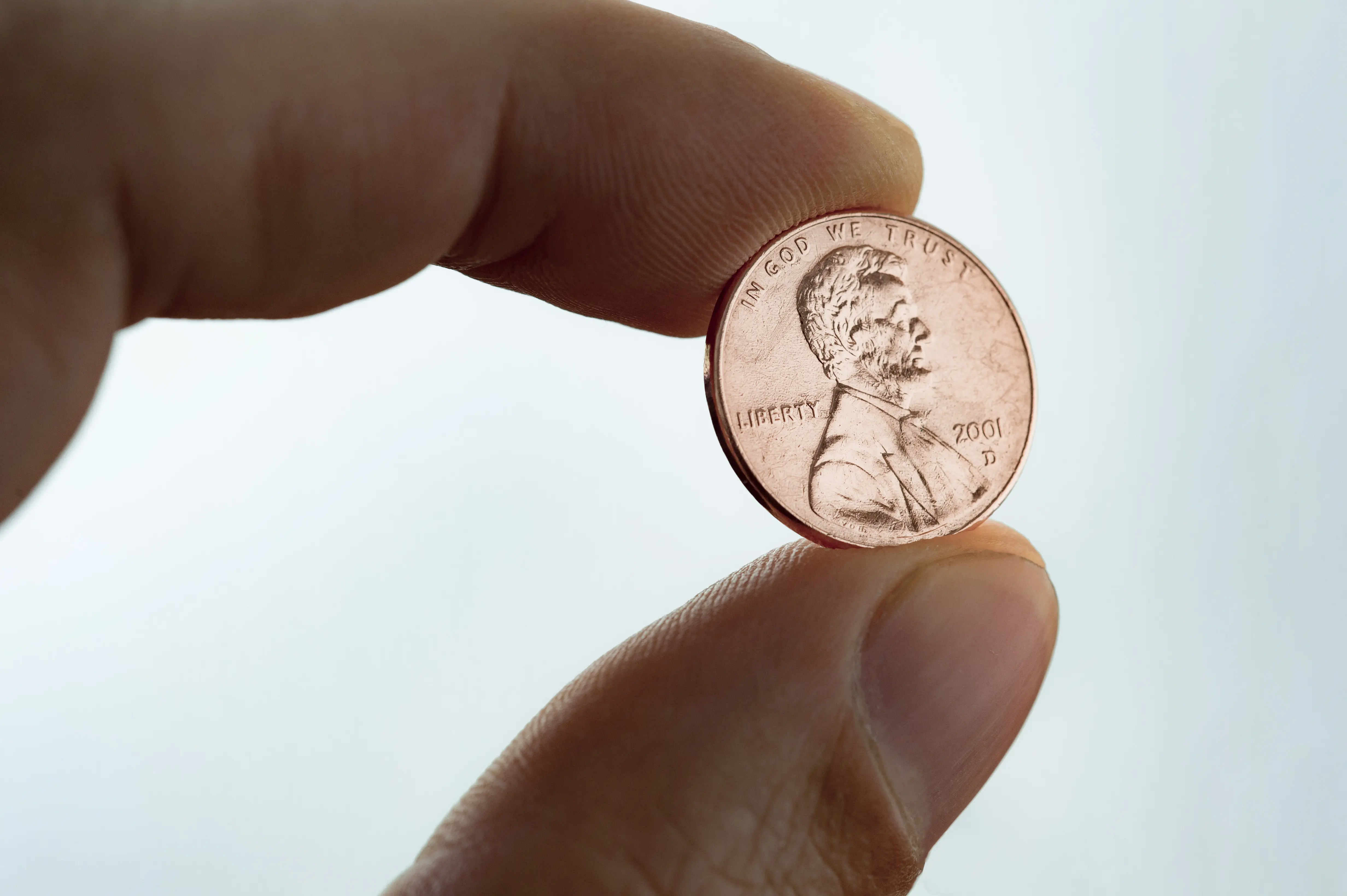 A close-up shot of a person's thumb and index finger holding a shiny copper Abraham Lincoln US penny coin