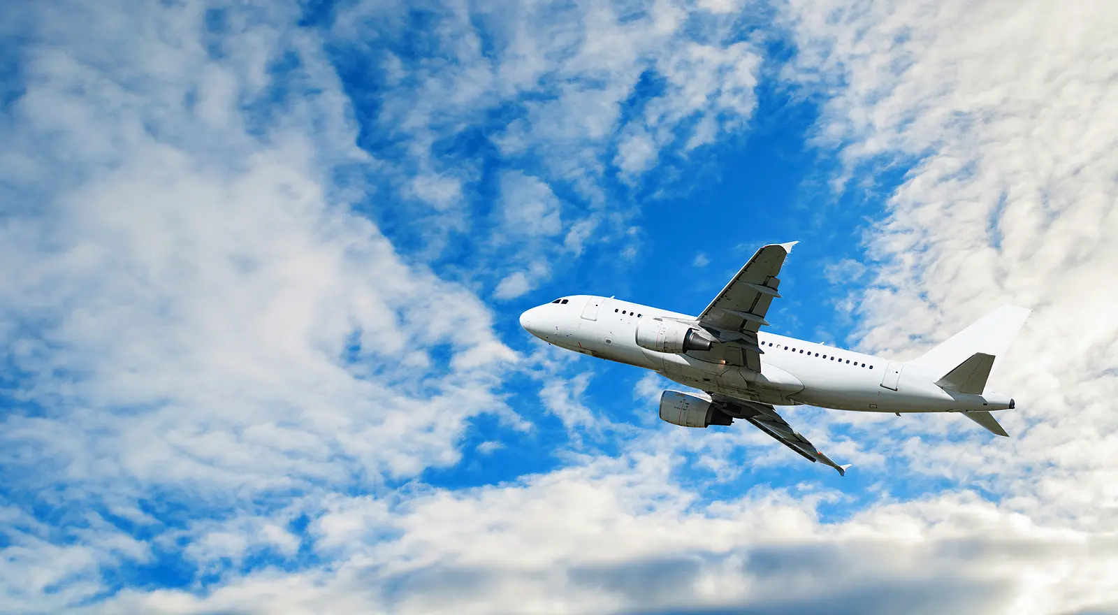 A commercial passenger airplane ascending during takeoff into a bright blue sky with white clouds, demonstrating principles of aerodynamics, lift, and aircraft design.