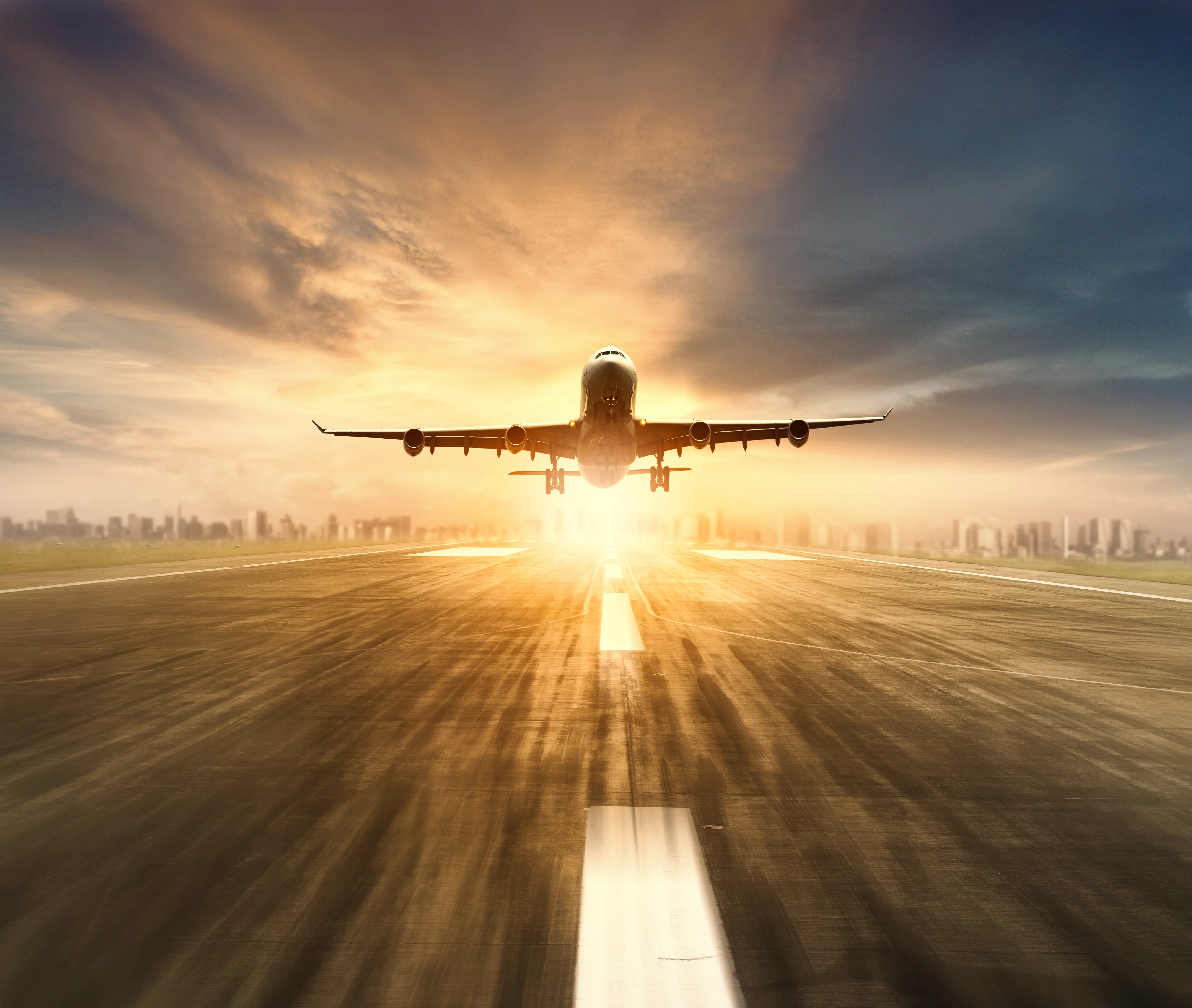 A commercial airplane taking off from an airport runway directly into a bright golden sunset with motion blur