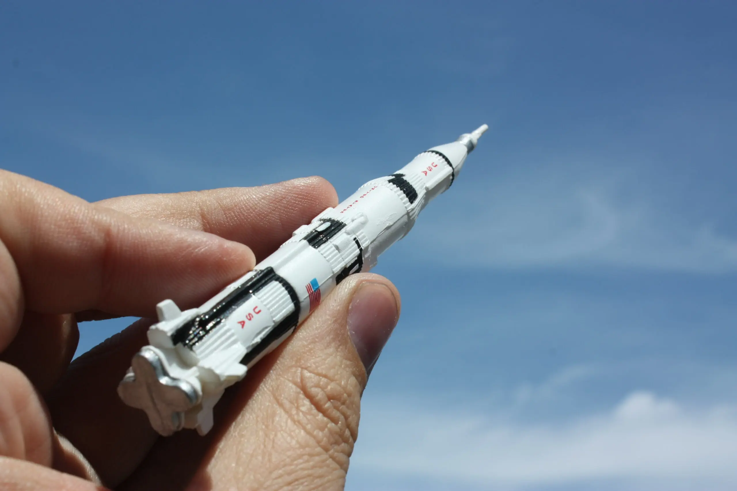 hand holding a miniature version of Apollo 11 pointing toward the sky.