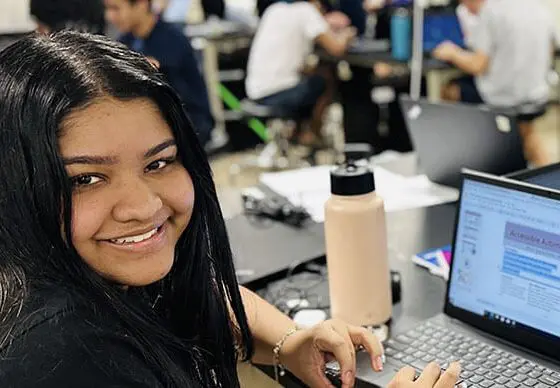 Smiling female student looking at the camera while working on a laptop in a classroom