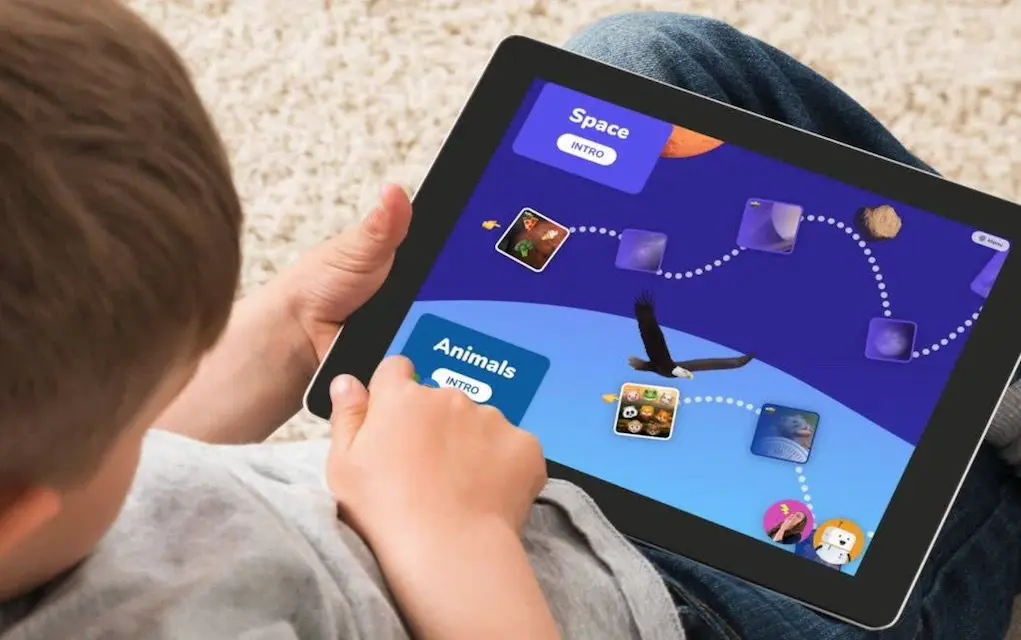 Over-the-shoulder view of a child using a tablet to navigate categories like Space and Animals on an interactive learning game app.