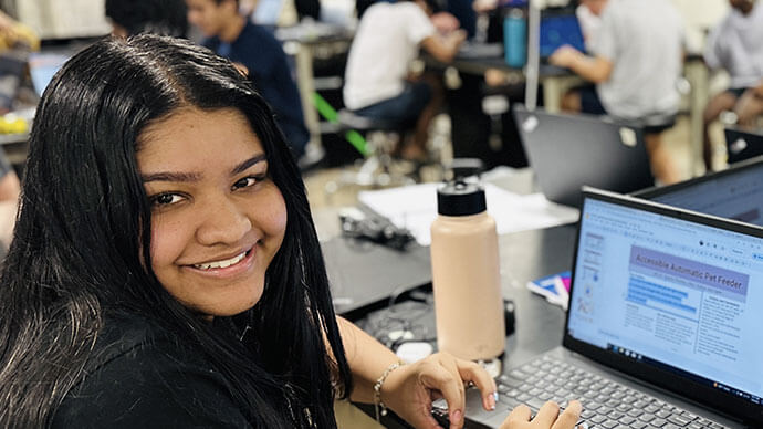 Smiling female student looking at the camera while working on a laptop in a classroom