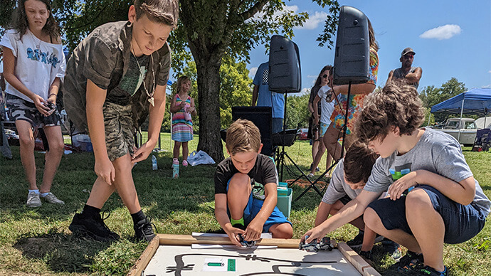 Four kids playing outdoors in nature with cars and a painted road