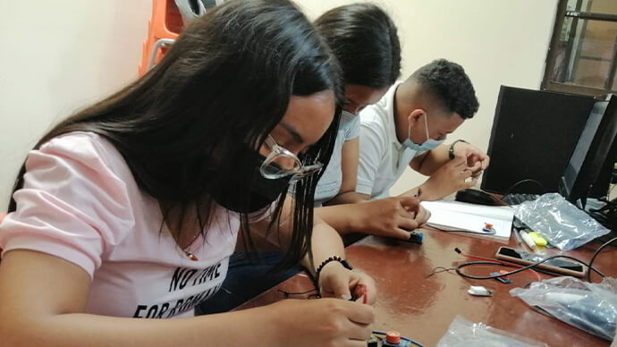 Three students use cables, tools, and connectors to build an engineering project