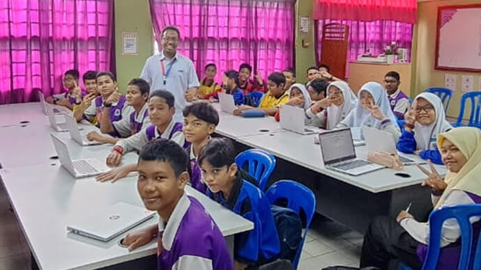 Classroom filled with kids and teacher smiling, all sitting down with laptops in front of them