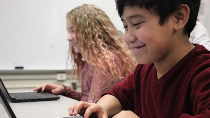 Two young students smiling and working on a laptop