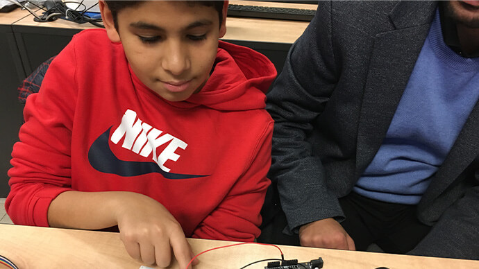 Boy pointing at semiconductor and microchip next to mentor teaching him about engineering