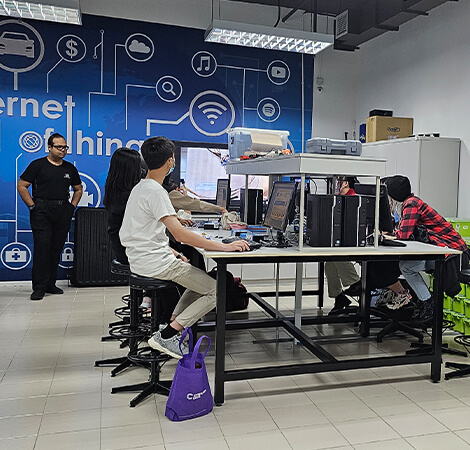 A group of students working on computers while an instructor assists them