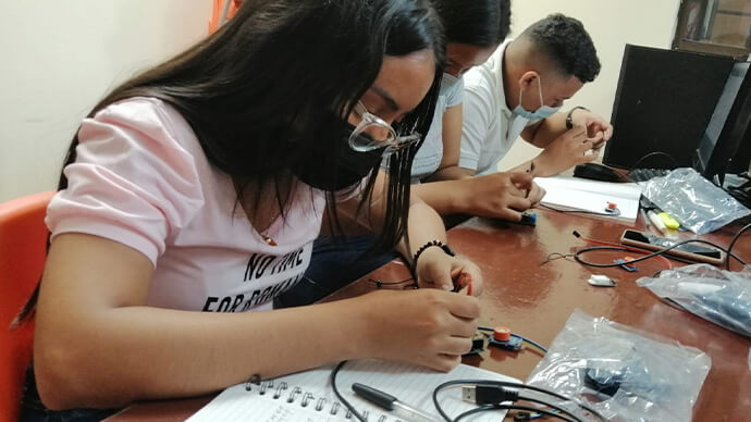 Three students use cables, tools, and connectors to build an engineering project