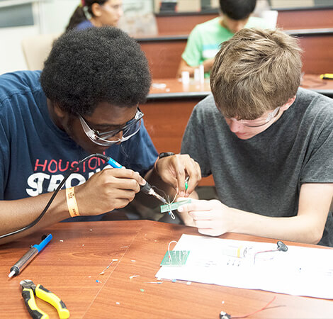 Two focused students soldering and collaborating