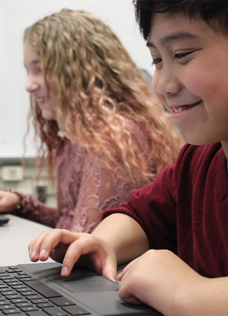 Two young students smiling and working on a laptop