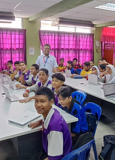 Classroom filled with kids and teacher smiling, all sitting down with laptops in front of them