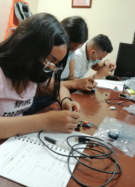 Three students use cables, tools, and connectors to build an engineering project.