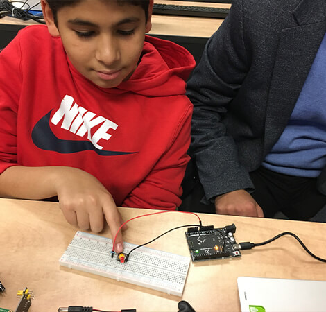 Boy pointing at semiconductor and microchip next to mentor teaching him about engineering